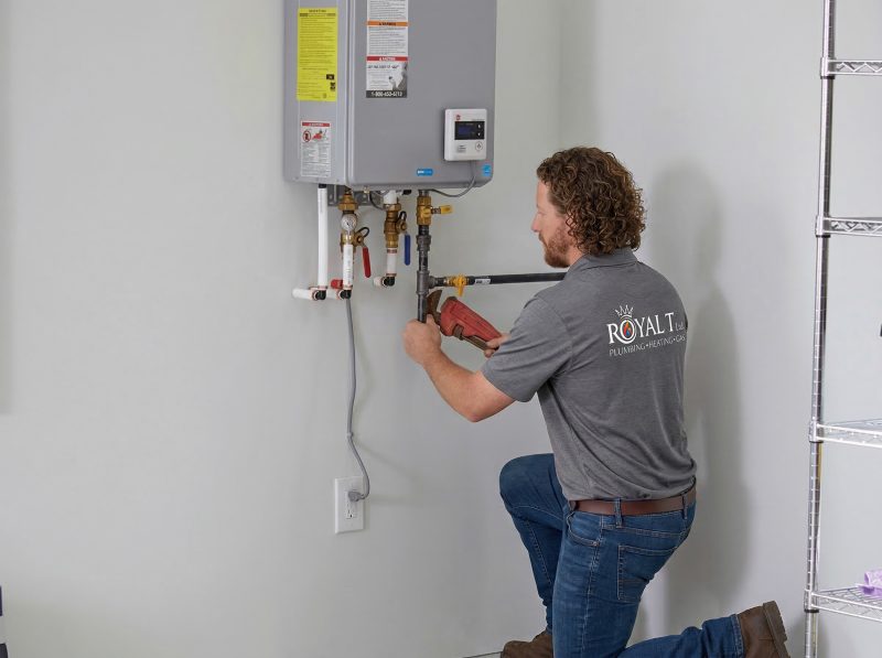 Plumber from Royal T Plumbing Heating and Gas Ltd. working on a water heater installation, featuring plumbing tools and equipment in a residential setting.