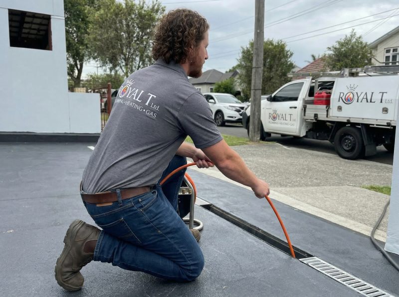 Plumber from Royal T Plumbing Heating and Gas Ltd. using a drain snake to clear a blockage in a residential drainage system.
